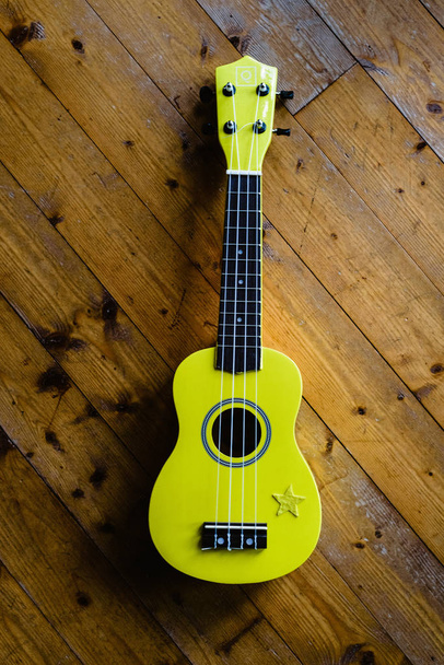 Piccolo ukulele giallo sul pavimento in legno pronto per essere giocato
 - Foto, immagini