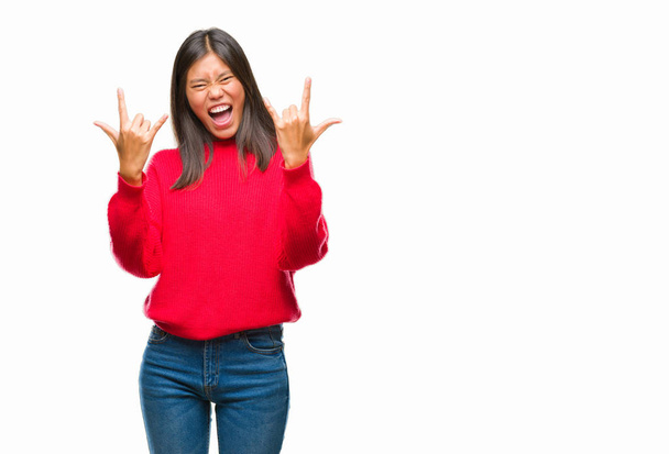 Jonge Aziatische vrouw winter trui dragen over geïsoleerde achtergrond schreeuwen met gekke expressie doen rock symbool met de handen omhoog. Muziek sterren. Zware concept. - Foto, afbeelding