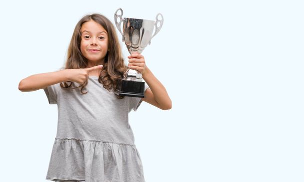 Brunette hispanic girl holding a trophy very happy pointing with hand and finger - Φωτογραφία, εικόνα