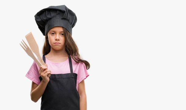 Brunette hispanic girl wearing cook uniform with a confident expression on smart face thinking serious - 写真・画像