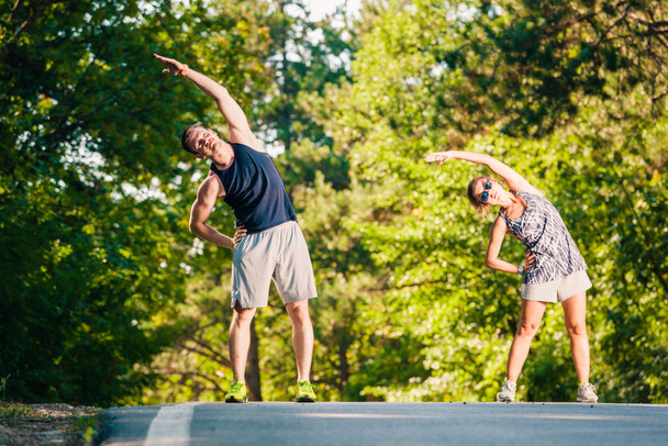 Athletic couple exercising on the road near the park - Photo, Image