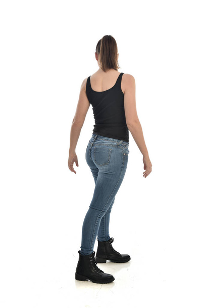 ritratto a figura intera di ragazza bruna che indossa singolo nero e jeans. In piedi in posa, di nuovo alla telecamera. isolato su sfondo bianco dello studio
. - Foto, immagini