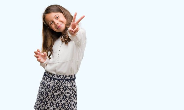 Brunette hispanic girl smiling looking to the camera showing fingers doing victory sign. Number two. - 写真・画像