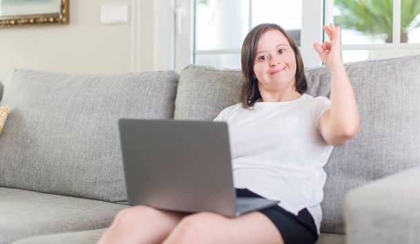 Down sendromu kadın evde parmak, mükemmel sembolü ile ok işareti yapıyor bilgisayar dizüstü kullanarak - Fotoğraf, Görsel