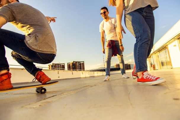 Grupo de amigos divirtiéndose con longboard al atardecer en la azotea
 - Foto, Imagen