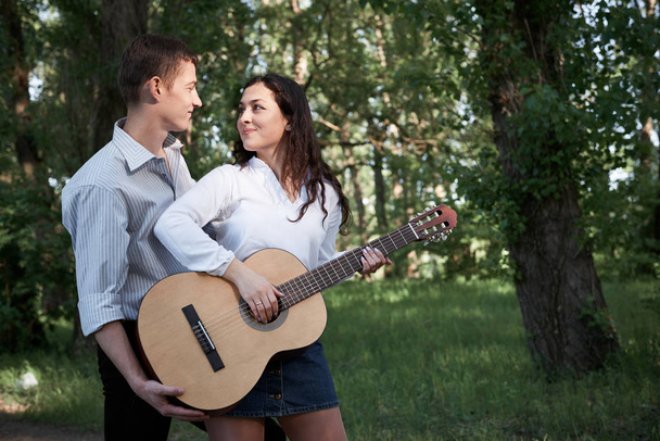young couple walking in the forest, playing guitar and dancing, summer nature, bright sunlight, shadows and green leaves, romantic feelings - Fotó, kép