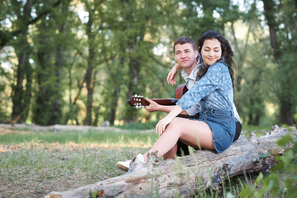 pareja joven sentada en un tronco en el bosque y tocando la guitarra, naturaleza de verano, sentimientos románticos
 - Foto, imagen