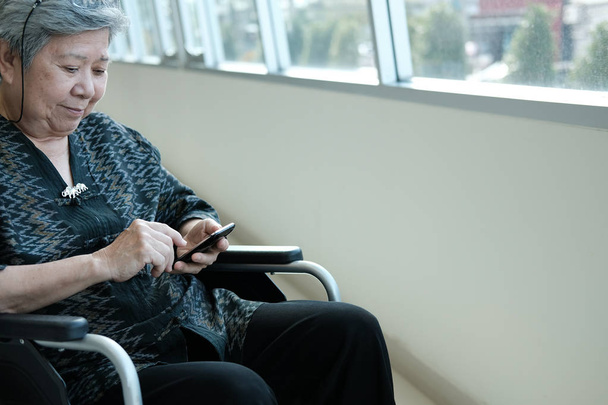 Starsza kobieta na wózku inwalidzkim, trzymając telefon komórkowy. podeszłym wieku senior tekstylny kobiece wiadomość, używając aplikacji z smartphone w domu - Zdjęcie, obraz