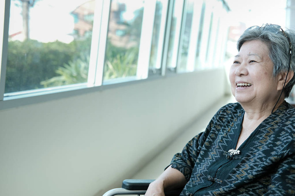 азиатская старшая женщина на инвалидной коляске улыбается и отдыхает у окна. счастливая пожилая женщина расслабляется в помещении. концепция зрелого образа жизни
 - Фото, изображение