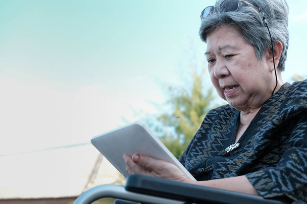 Starszy rangą kobieta na wózku inwalidzkim, trzymając tablet. starszych kobiet SMS wiadomość, używając aplikacji z touchpad w ogrodzie - Zdjęcie, obraz