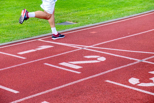 Patas corriendo y sombra en movimiento de un atleta masculino corriendo en pista de estadio exterior
. - Foto, imagen