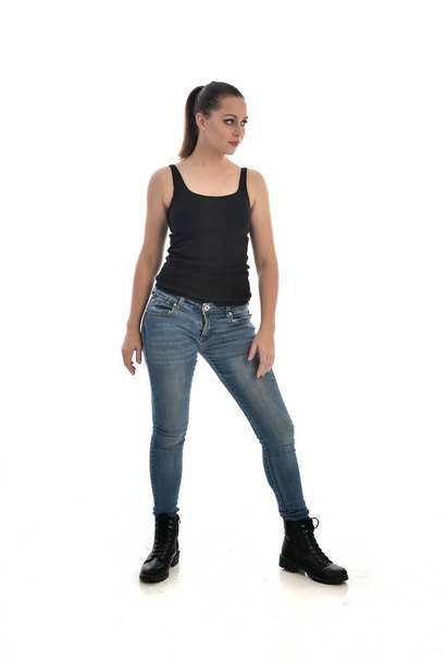 ritratto a figura intera di ragazza bruna che indossa singolo nero e jeans. in piedi posa. isolato su sfondo bianco dello studio
. - Foto, immagini