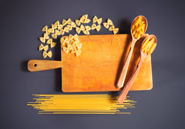 Cutting board and raw pasta on dark background. - Фото, изображение
