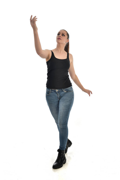Ganzkörperporträt eines brünetten Mädchens mit schwarzem Single und Jeans. Stehende Pose. isoliert auf weißem Studiohintergrund. - Foto, Bild