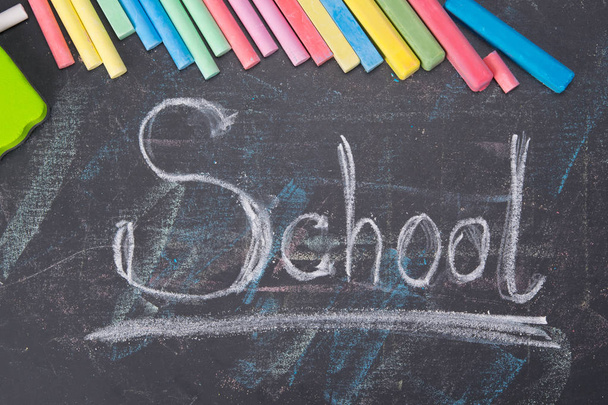 on the background of a black board, the word school is written, surrounded by colored crayons - Foto, Imagen