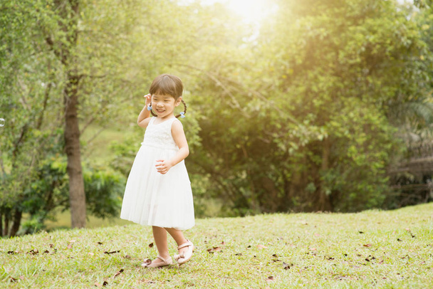 Happy little girl playing at green park. Asian family outdoors portrait. - Φωτογραφία, εικόνα