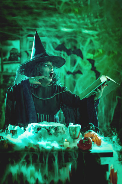 Witch with awfully face reading recipe of magic drink, Halloween concept - Photo, Image