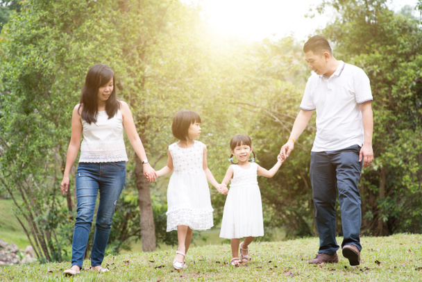 屋外のアジア家族。親と子が手を繋いでいると、緑豊かな公園でウォーキング.  - 写真・画像