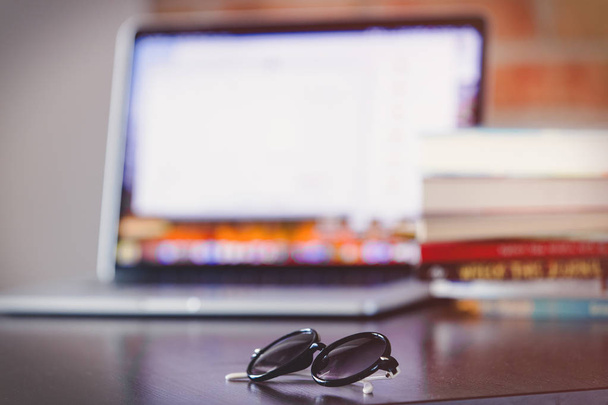 sunglasses on a table with laptop computer and books on brick wall background - Foto, Imagem