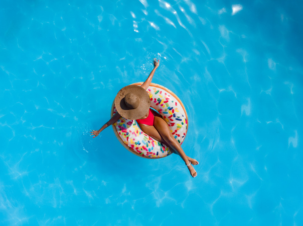 Vista superior da mulher nova na piscina no donut inflável do anel
 - Foto, Imagem