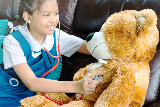 little girl is smiling and playing doctor with brown bear and stethoscope. Kid and health care concept. - Photo, Image
