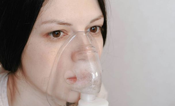 Use nebulizer and inhaler for the treatment. Closeup young womans face inhaling through inhaler mask. Side view. - Foto, afbeelding