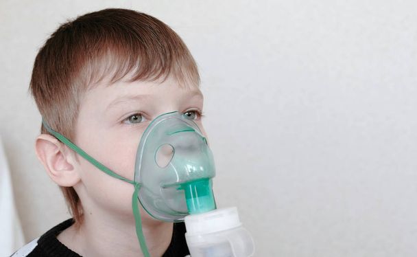 W leczeniu za pomocą rozpylacza i inhalator. Chłopiec wdechu przez inhalator maski. Widok z przodu - Zdjęcie, obraz