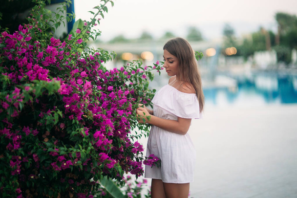 молодая и красивая девушка в летнем городе, стоящая рядом с цветами
 - Фото, изображение