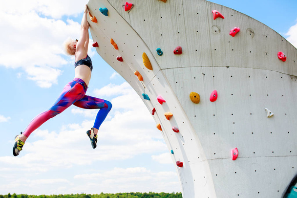 Photo of sporty blonde in leggings hanging on wall for rock climbing against blue sky - Fotografie, Obrázek
