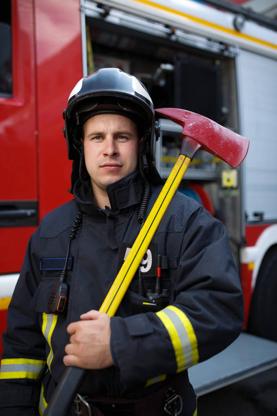 Photo of serious fireman with ax on background of fire engine - Foto, Bild