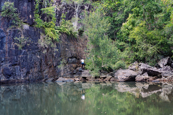 A hiker set to climb the face of a rock wall behind a green pool in a forest - Photo, Image