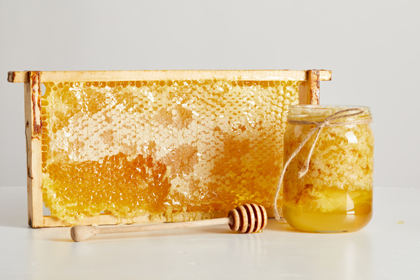 vista de cerca de la miel de madera más profunda, tarro de vidrio con miel y pila de cera de abejas en la mesa blanca
 - Foto, imagen