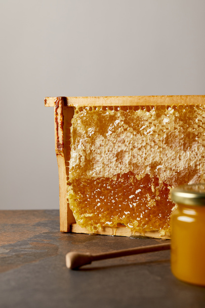 close up view of glass jar with honey, beeswax and wooden honey deeper on grey background - Valokuva, kuva