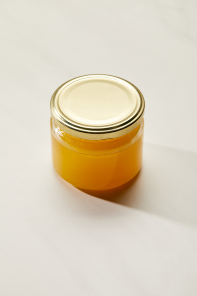 close up view of sweet organic honey in glass jar on white surface - Foto, afbeelding