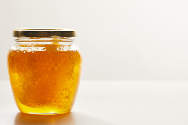 close up view of honey and beeswax in glass jar on white background - Foto, imagen