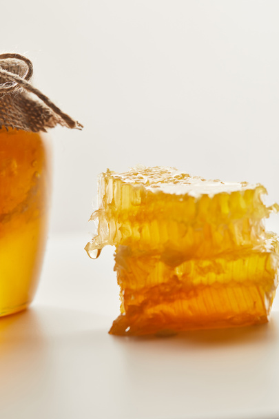 close up view of pile of beeswax and glass jar with honey on white tabletop - Foto, Imagen