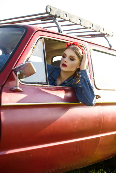 Girl dressed in denim clothes driving red old car - Fotoğraf, Görsel