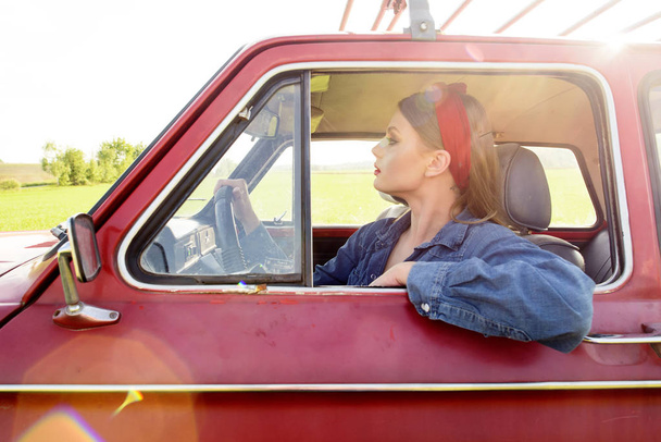 Girl dressed in denim clothes driving red old car - Foto, afbeelding