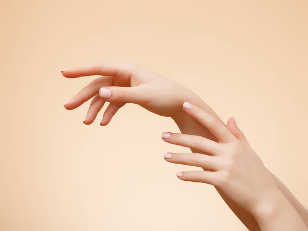Крупным планом изображение рук красивой женщины со светло-розовым маникюром на ногтях. Уход за кожей рук, маникюр и косметические процедуры. Элегантные и изящные руки с тонкими изящными пальцами
 - Фото, изображение