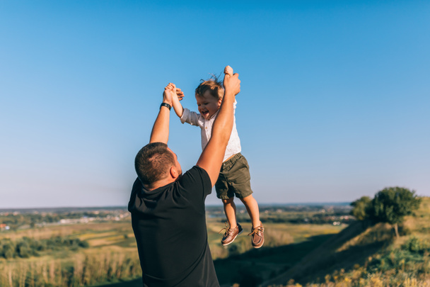 padre joven jugando y divirtiéndose con el pequeño hijo feliz al aire libre
 - Foto, Imagen