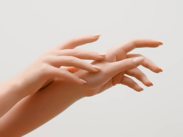 Nahaufnahme Bild der schönen Frauenhände mit hellrosa Maniküre auf den Nägeln. Hautpflege für Hände, Maniküre und Schönheitsbehandlungen. elegante und anmutige Hände mit schlanken, anmutigen Fingern - Foto, Bild