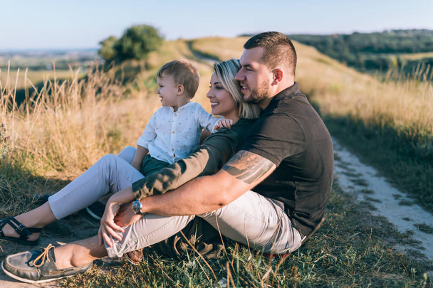 happy parents with adorable little son sitting and looking away in rural landscape - Фото, изображение