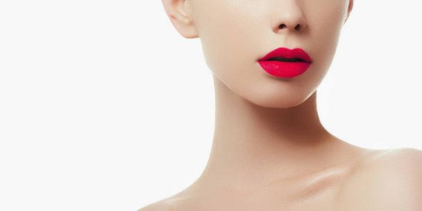 Καλλυντικά, μακιγιάζ και τάσεις. Φωτεινό lip gloss και κραγιόν στα χείλη. Closeup όμορφο θηλυκό πρόσωπο με κόκκινα χείλη μακιγιάζ. Πανέμορφο μέρος του γυναικείου προσώπου. Τέλεια καθαρό δέρμα στο κόκκινο φως - Φωτογραφία, εικόνα