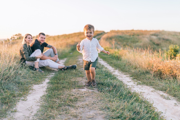 happy parents looking at adorable smiling little son running on trail - Photo, Image
