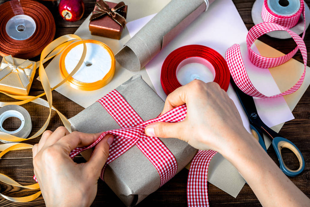 Wrapping christmas gift with paper, detail of hands and ribbons for packing presents - Photo, Image