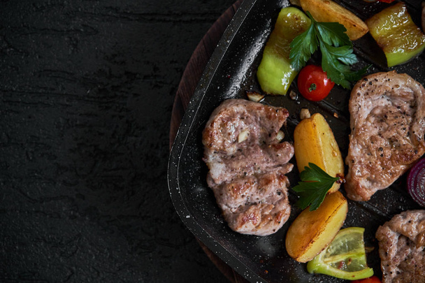 Roasted pork steaks fillet in frying pan over dark background. View from above - Photo, Image