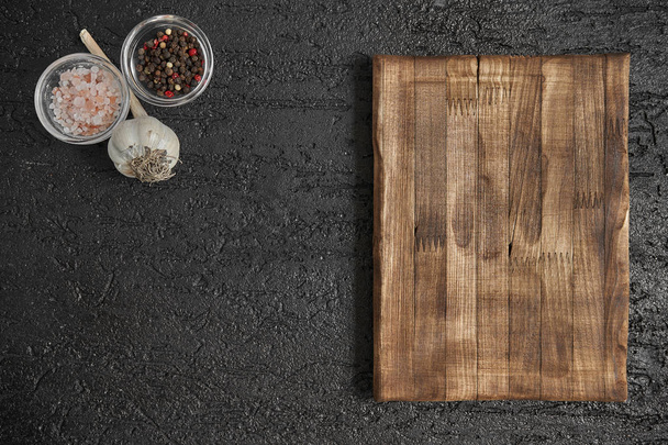 Round wooden cutting board on black table. Top view of empty kitchen trendy rustic wooden tray. Copy space for text. Food and menu background. - Фото, зображення
