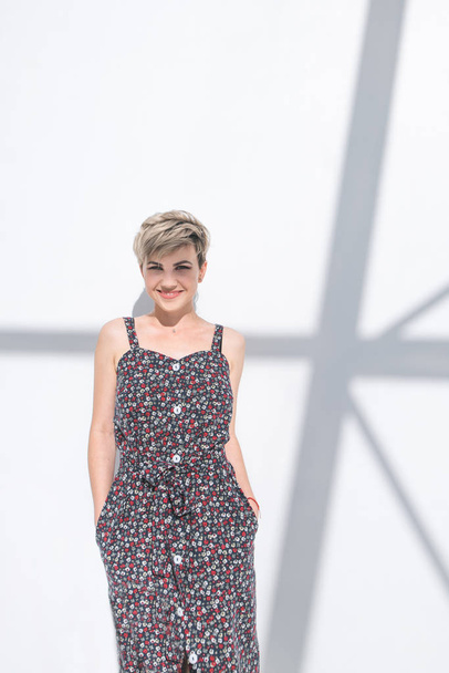 Portrait of a happy fashionable woman in stylish clothes in a light room on a white background with shadows. Smiling stylish woman with short hair poses against the backdrop of a white abstract wall. - Foto, immagini