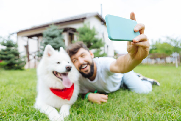 Smiling man holding his blue smart phone making photo with husky - Foto, Bild