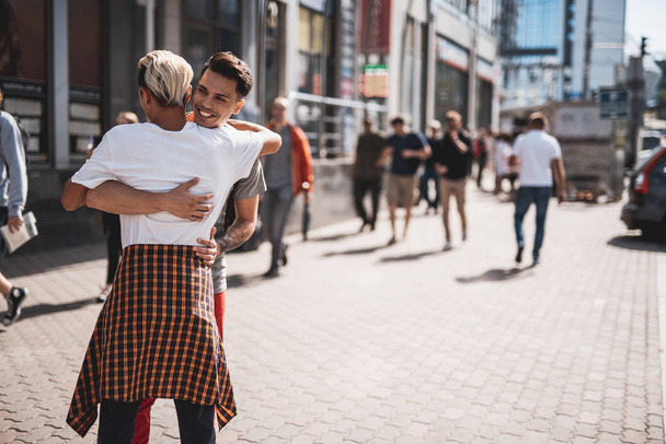 Positive male hugging comrade during walk outdoor - Photo, Image